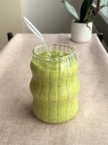 Close-up of the green smoothie in the ridged glass, highlighting tiny seed specks in the drink.