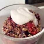 Dollop of creamy yogurt atop baked berry crumble in a glass bowl.