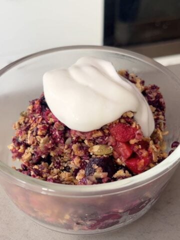 Dollop of creamy yogurt atop baked berry crumble in a glass bowl.