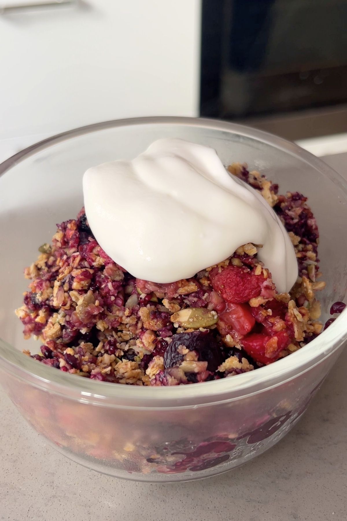 Dollop of creamy yogurt atop baked berry crumble in a glass bowl.