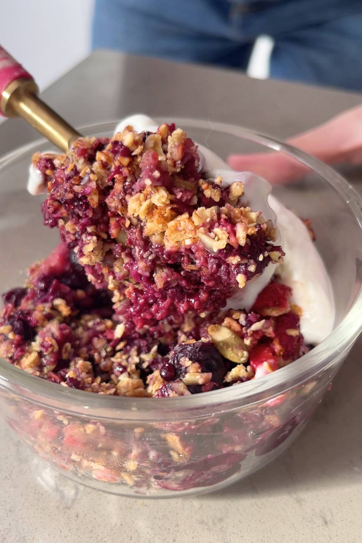 Spoon holding a bite of berry crumble with crisp oat topping over a plate.