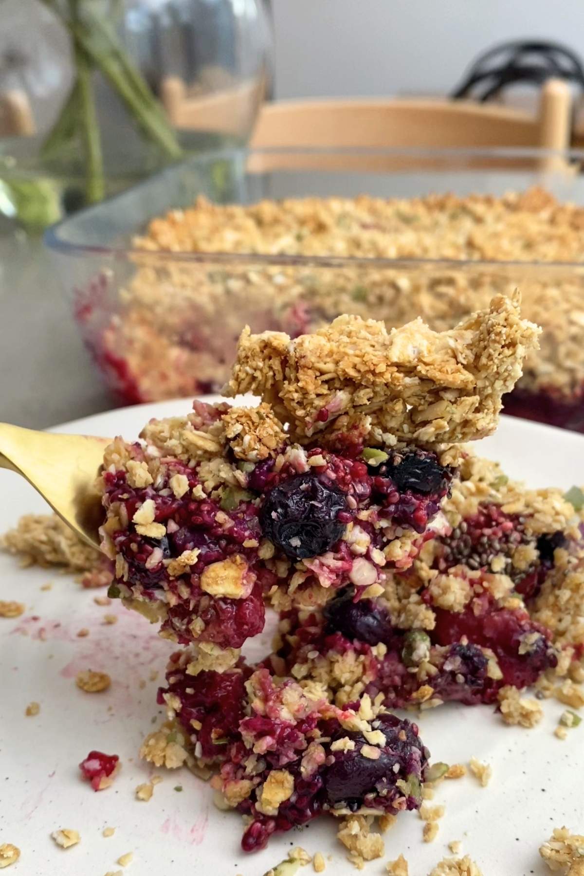 Spoon lifting a scoop of berry crumble and yogurt from a glass bowl.