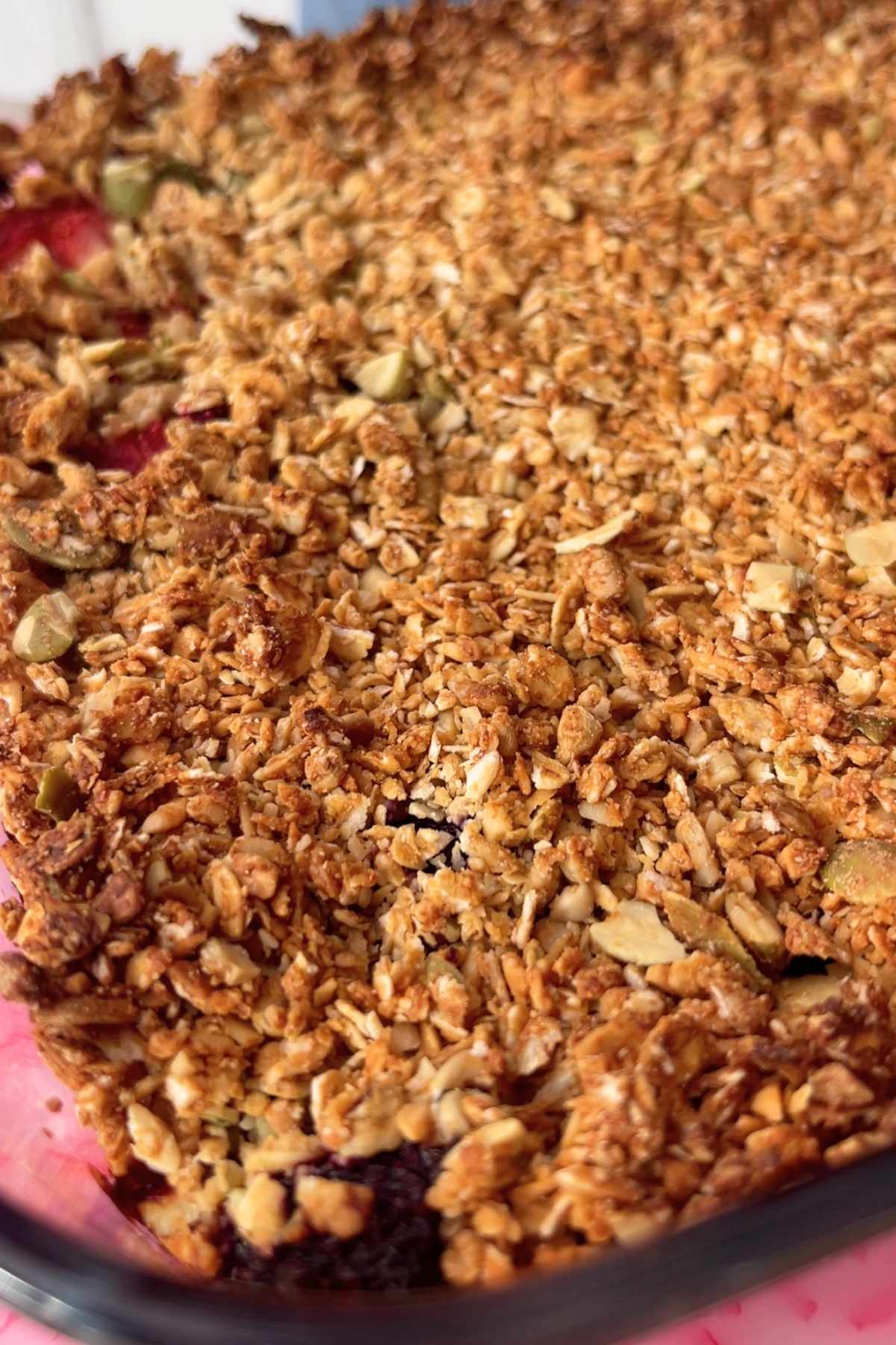 Close-up of golden-brown oat crumble with pumpkin seeds over berry filling.