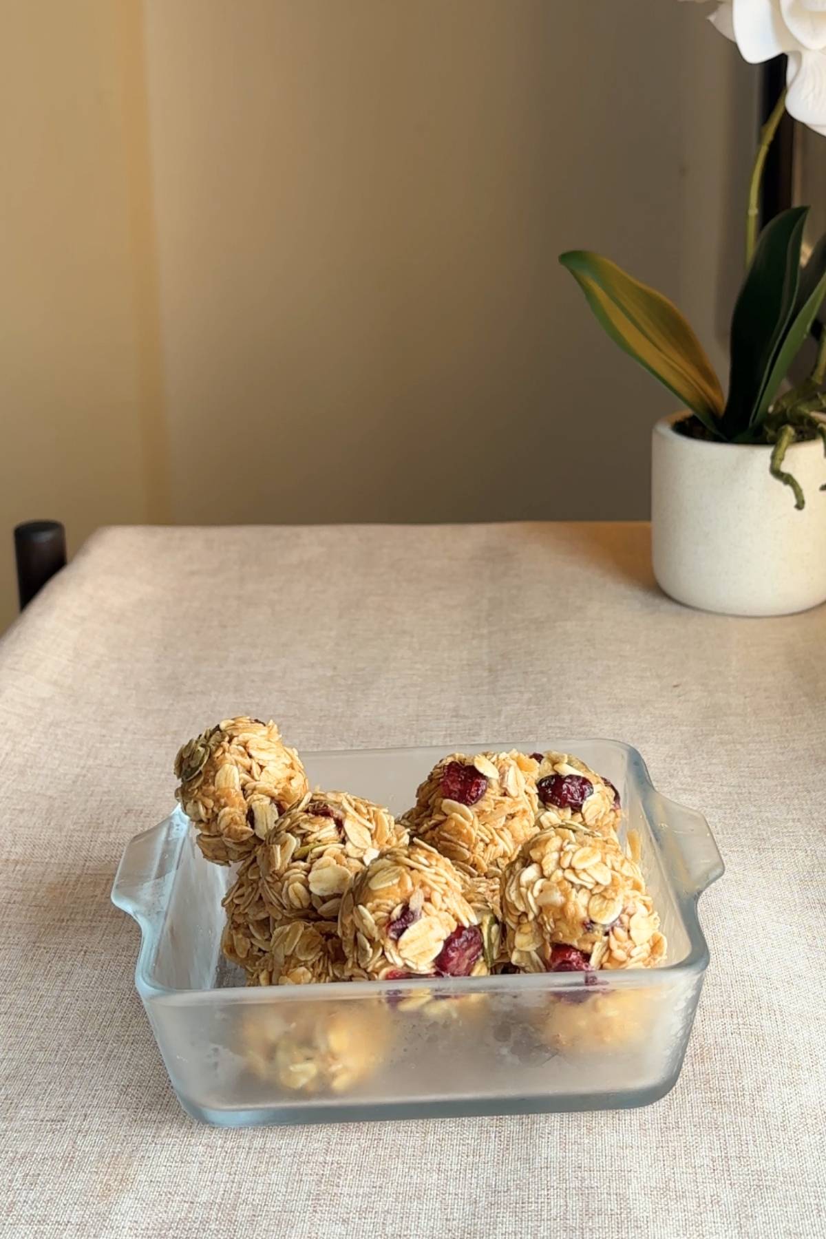 Glass dish filled with oat and cranberry balls sitting on a neutral tablecloth.
