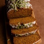 Sliced pumpkin loaf with white glaze and pepitas on top, arranged on a wooden board.