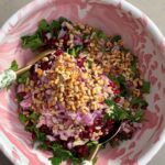 Chopped parsley, red onion, toasted almonds, and pomegranate seeds piled over mixed grains in a swirl bowl.