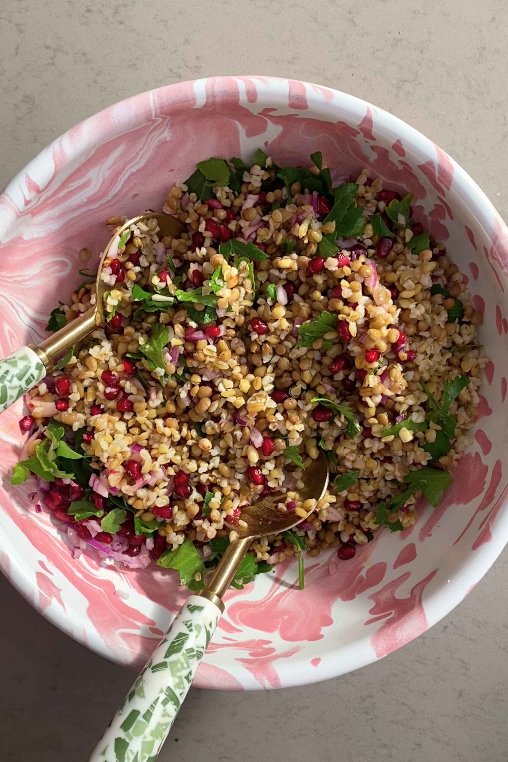 Mixed grains and lentils dotted with parsley leaves and pomegranate seeds in a marbled serving bowl.