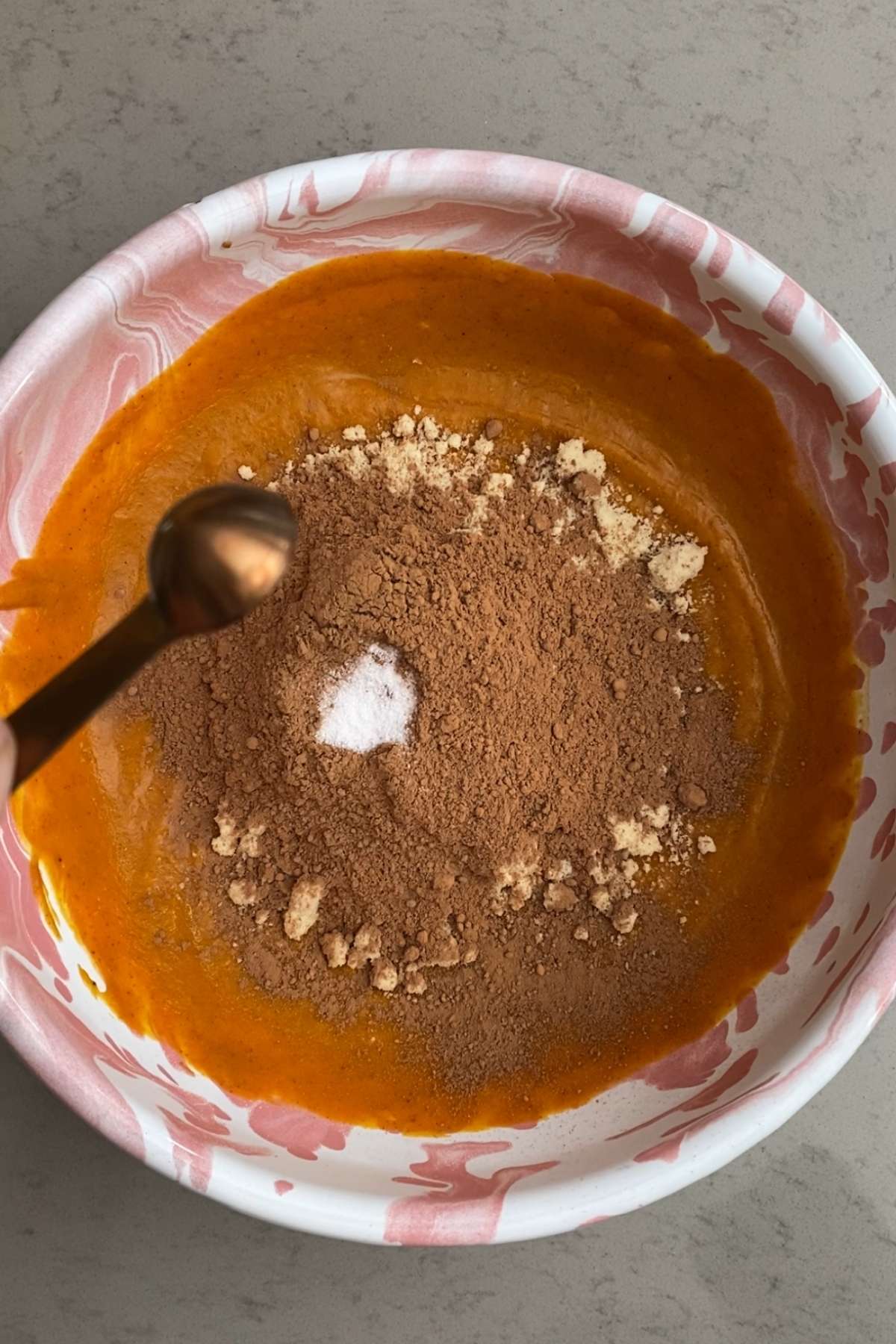 Cocoa powder, almond flour, and salt sprinkled over a blended pumpkin mixture in a marbled mixing bowl.