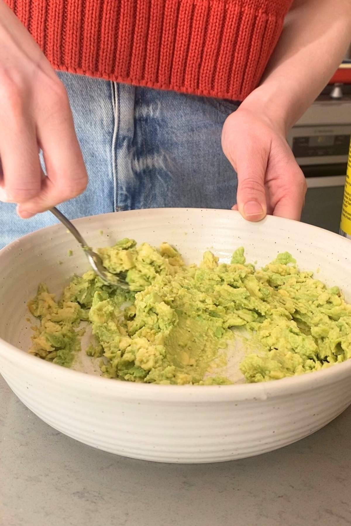 Person mashing avocado in a large white bowl with a fork.