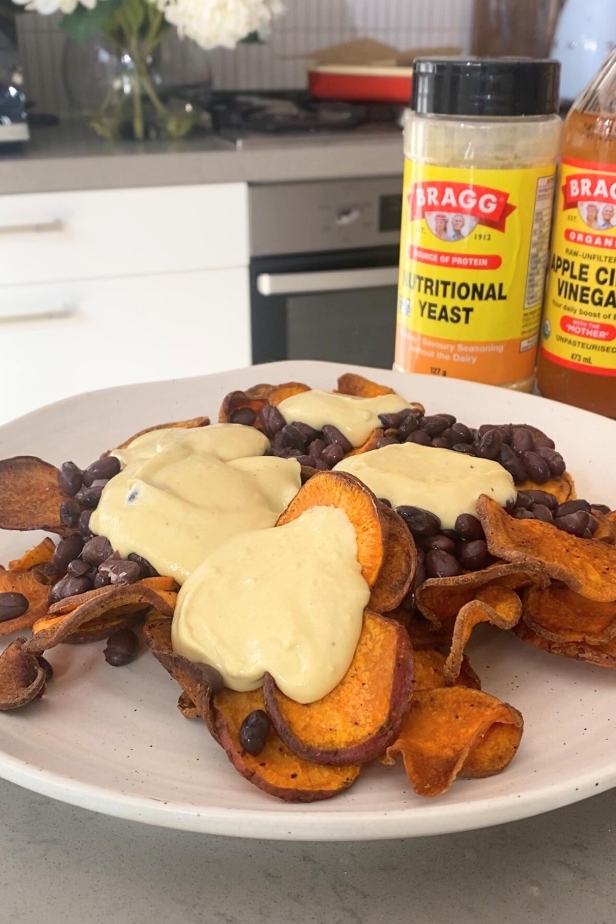 Sweet potato chips topped with creamy sauce and black beans on a white plate.