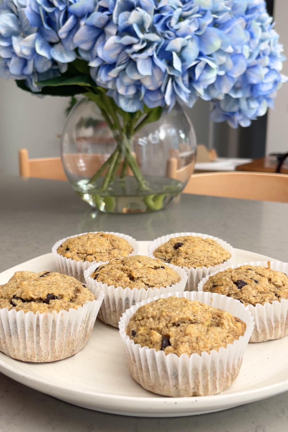 Six golden-brown muffins rest on a white plate.