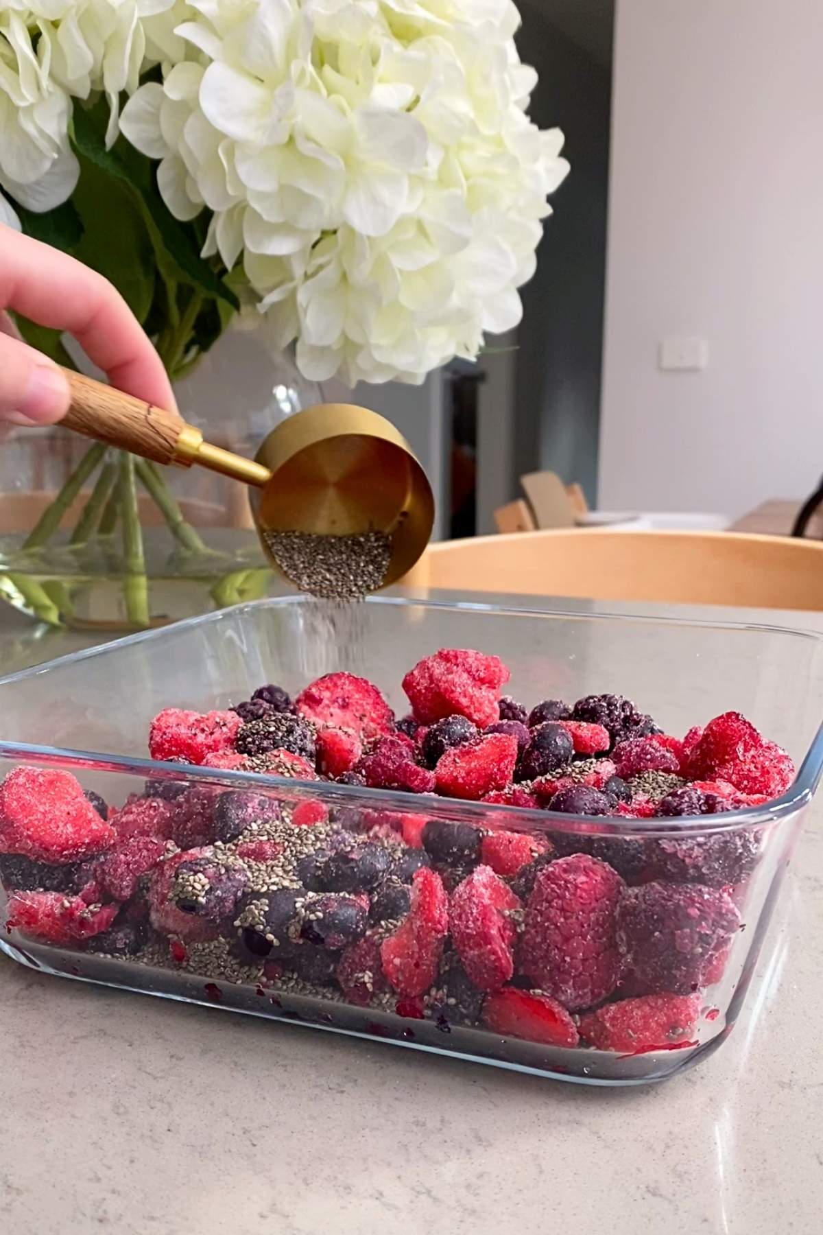 Hand sprinkling chia seeds over frozen berries in a glass baking dish.