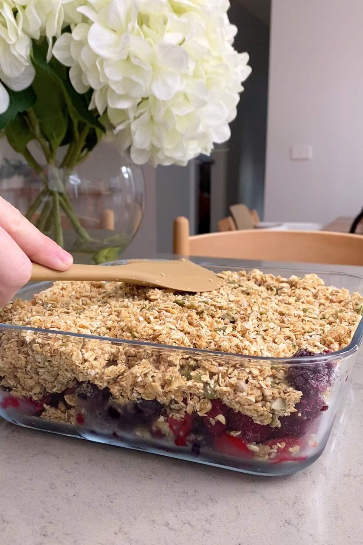 Spatula smoothing oat crumble topping over berries in a baking dish.