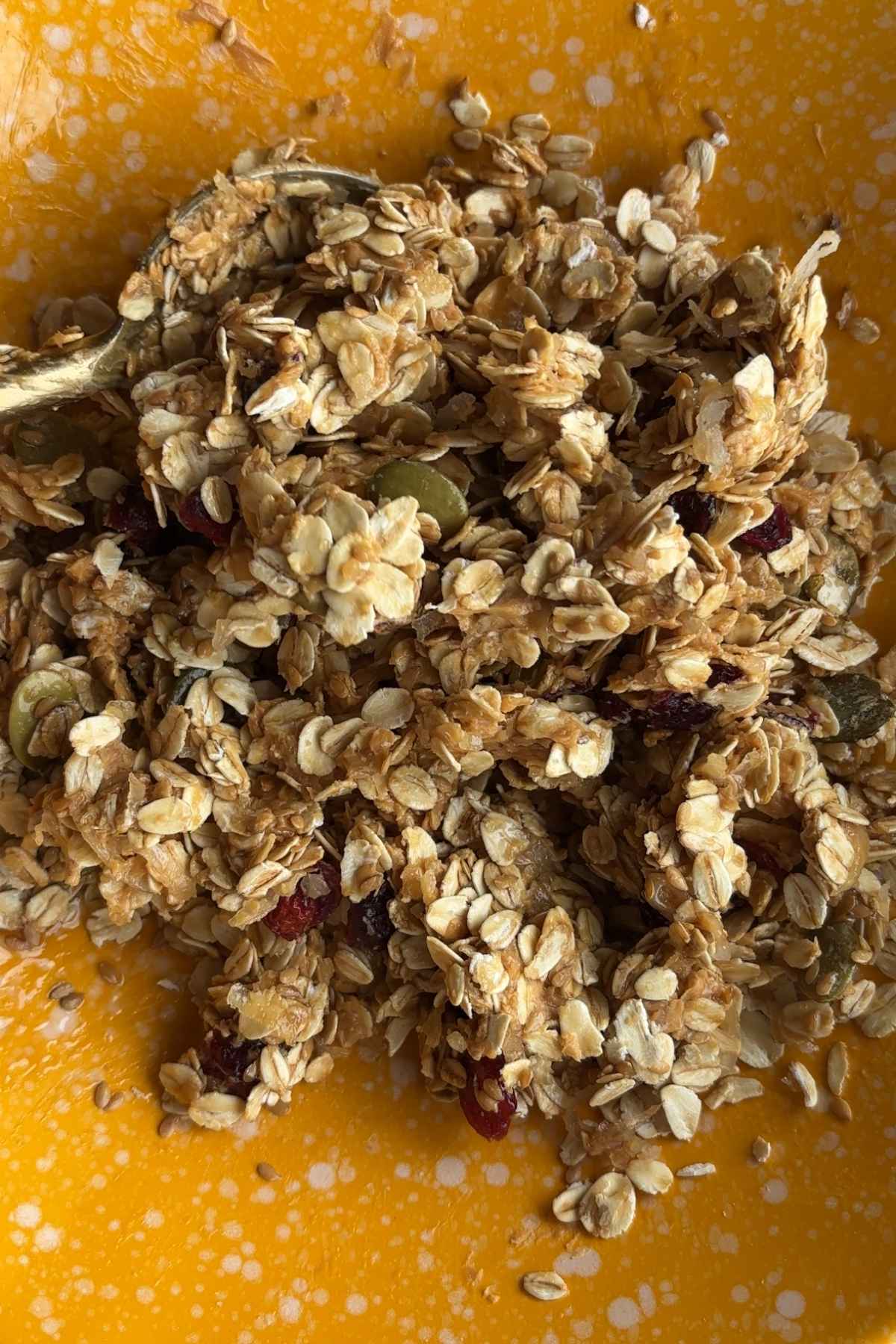 Sticky oat mixture with visible cranberries and pepitas in a yellow bowl.