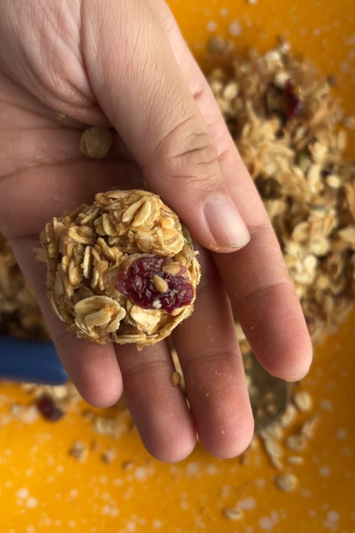 A hand holding a rolled oat ball with a visible dried cranberry pressed into the surface.