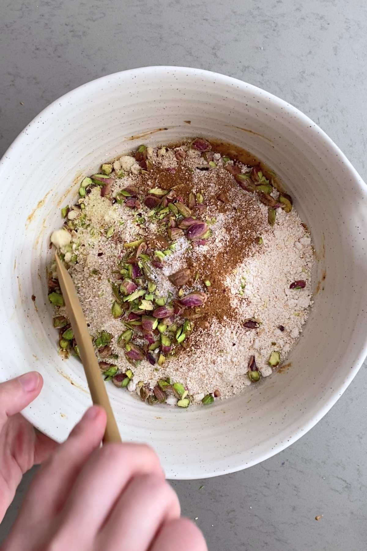 A white bowl with almond flour, chopped pistachios, and cinnamon layered over banana mixture.