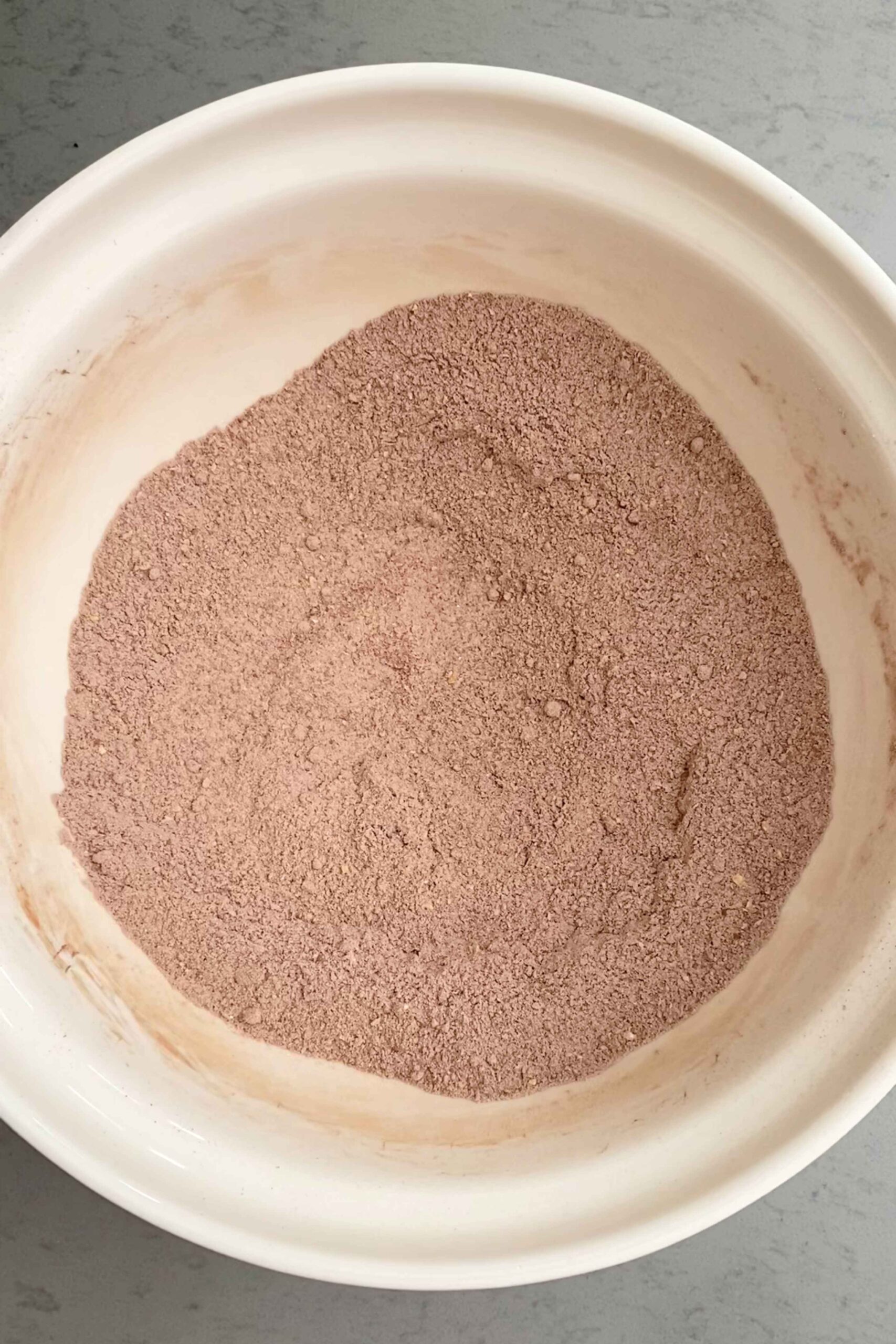 White mixing bowl filled with light brown cocoa-speckled dry mixture.
