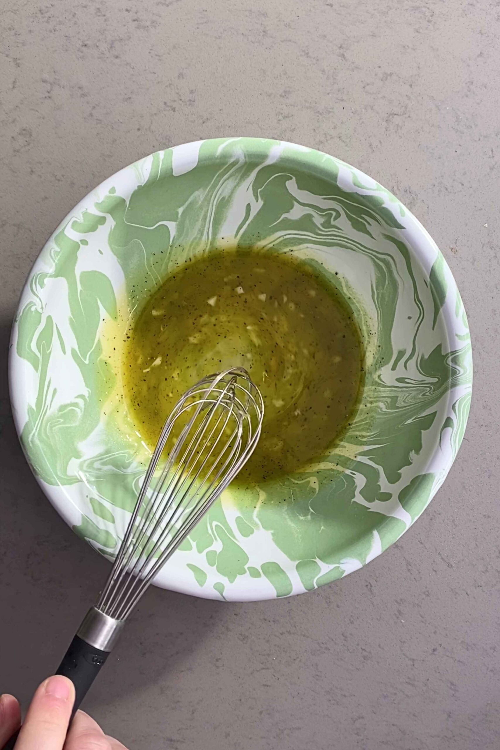 A whisk resting in a green-and-white bowl of lemony vinaigrette.