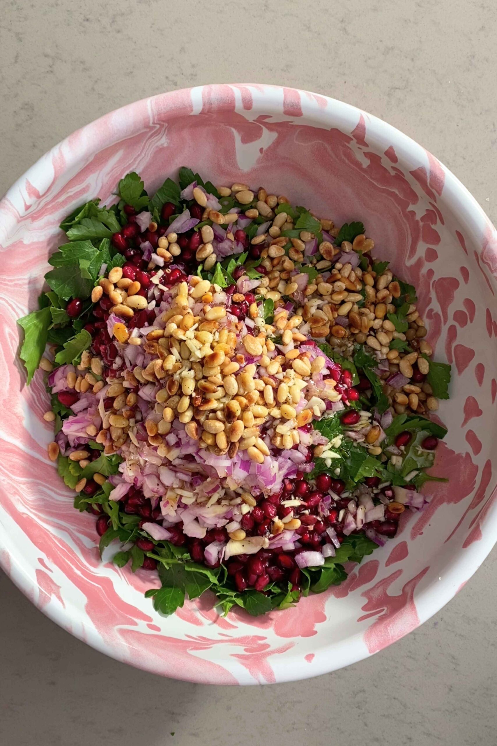 Chopped parsley, red onion, pomegranate seeds, and toasted almonds piled in a bowl.