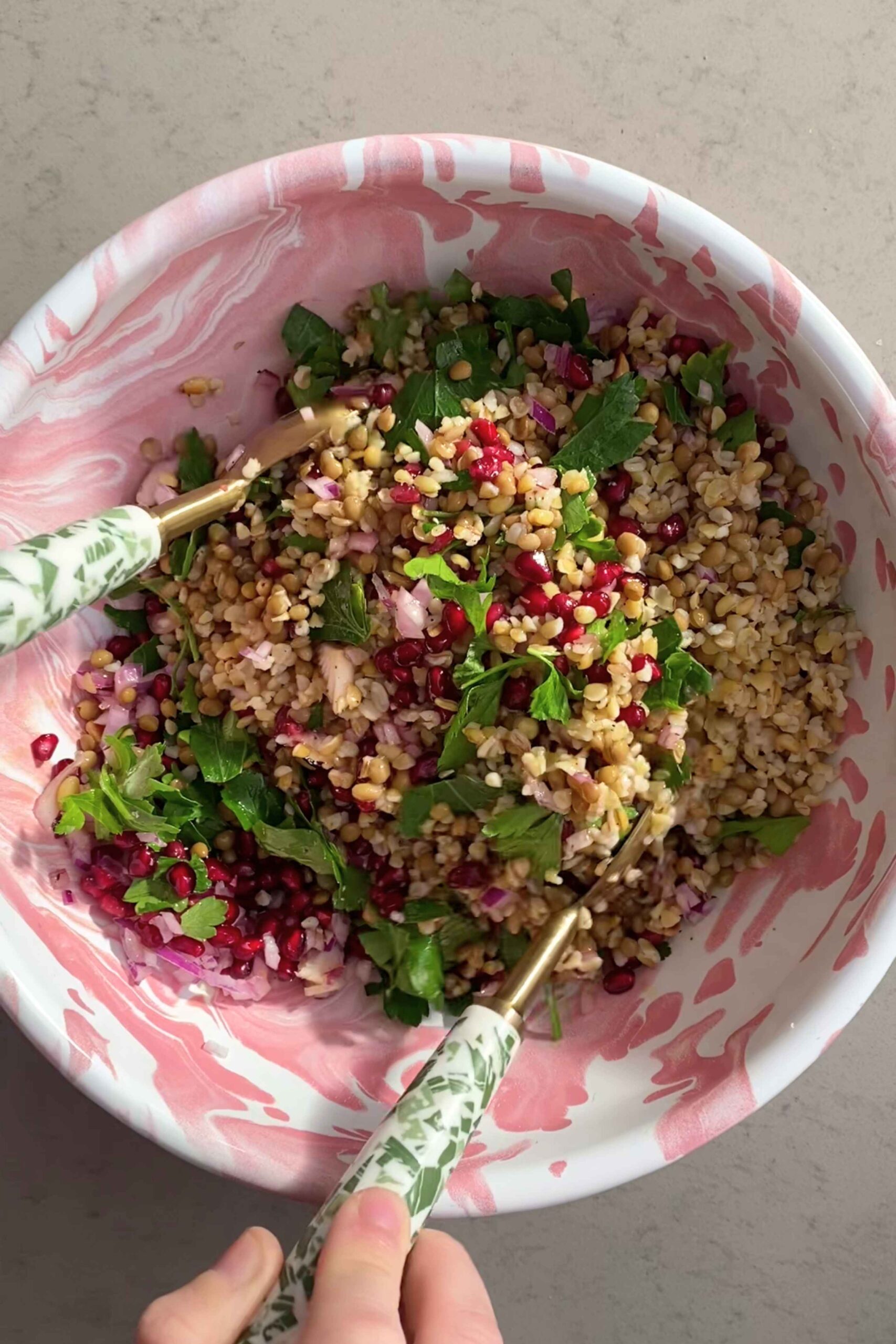 Freekeh and lentil mixture being stirred with patterned salad servers.