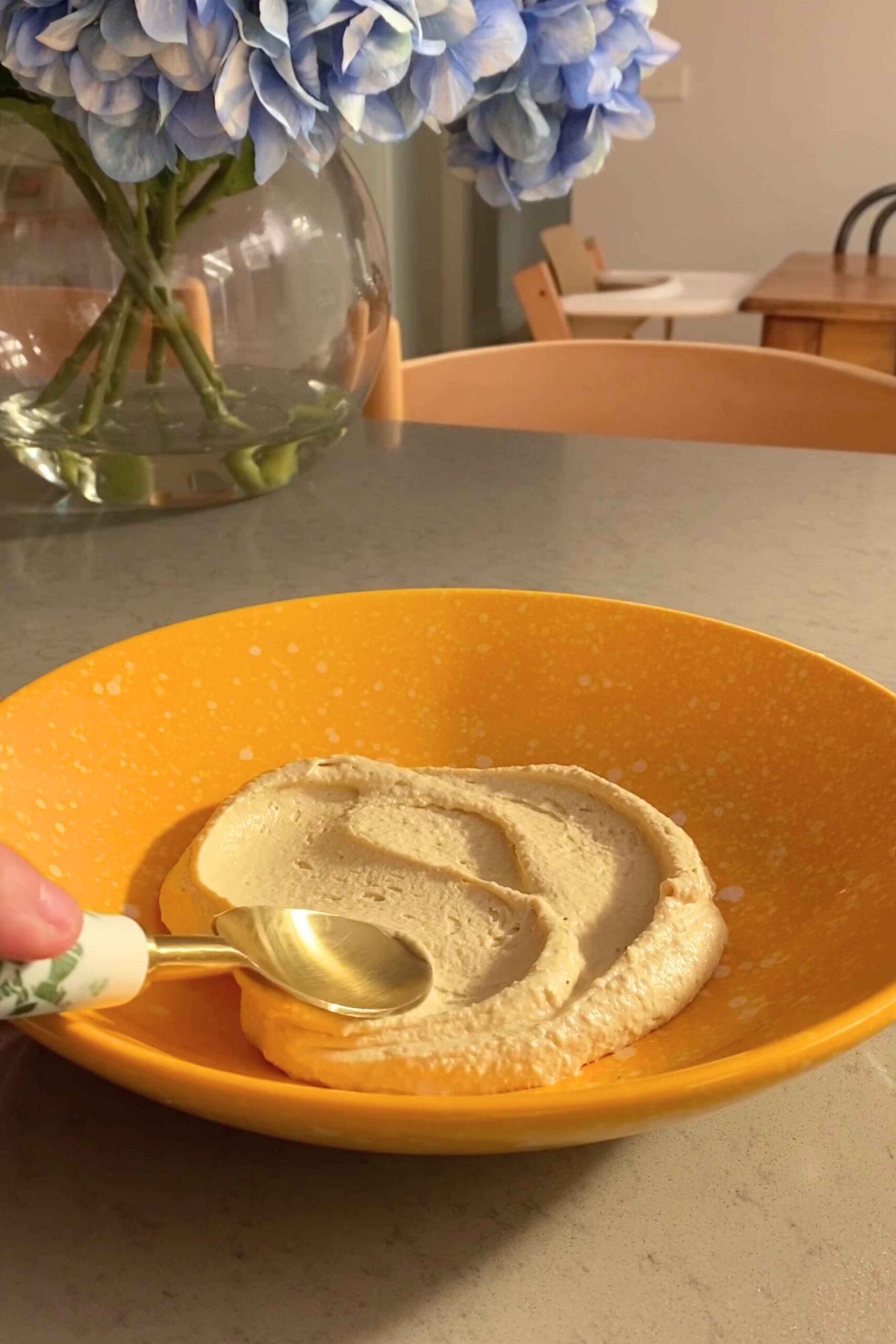A smooth layer of hummus spread across a yellow bowl.