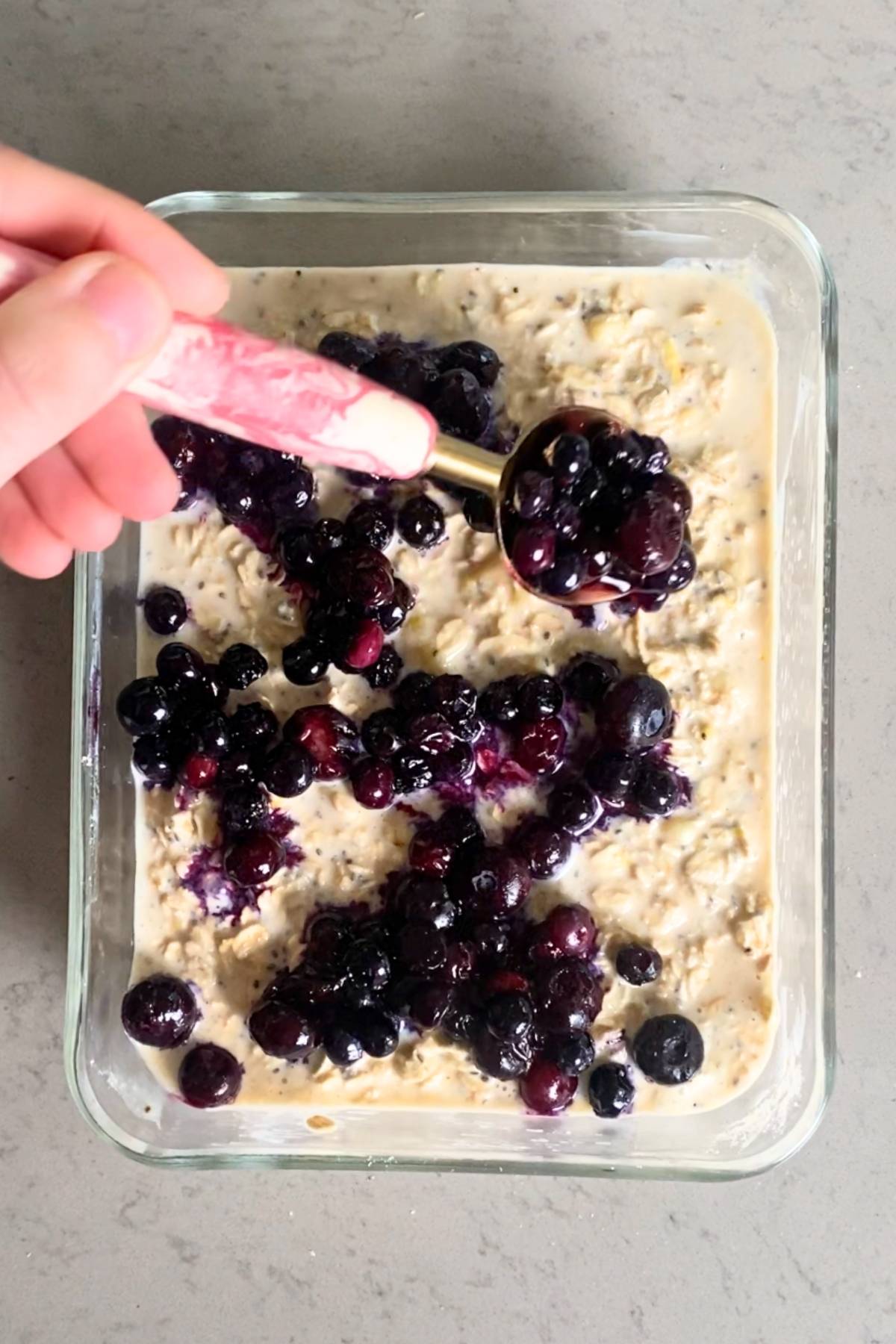 Cooked blueberries being spooned over oat mixture in a glass baking dish.