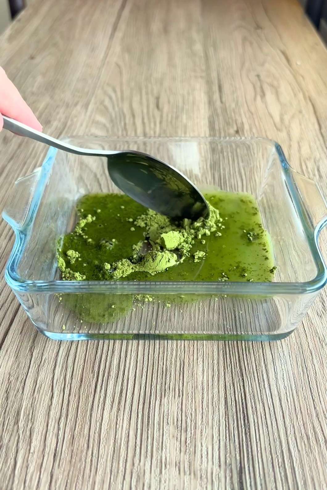Spoon mixing bright green matcha paste in a glass container.