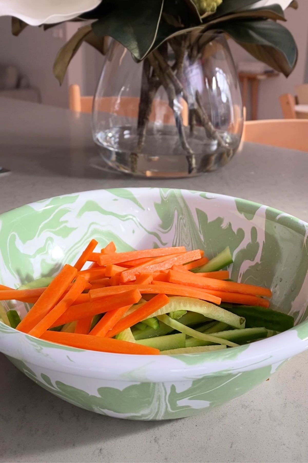 Thin cucumber and carrot strips sit in a marbled mixing bowl.