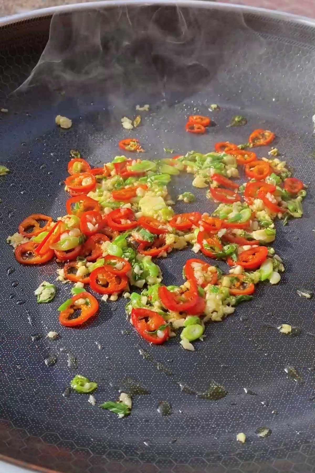 Sliced red chilies, minced garlic, and green onion sizzling in a wok.