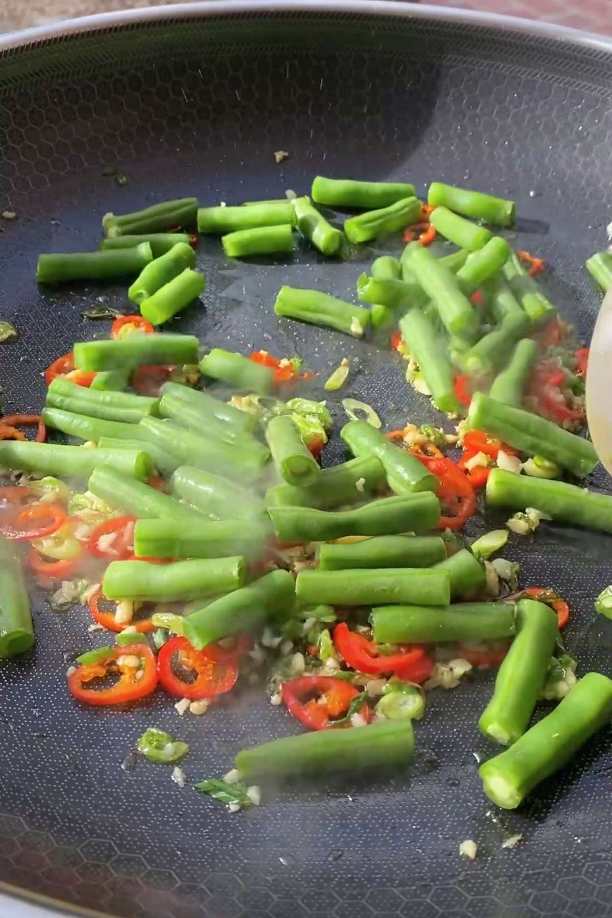 Bright green beans added to the fragrant chili-garlic mixture in a pan.