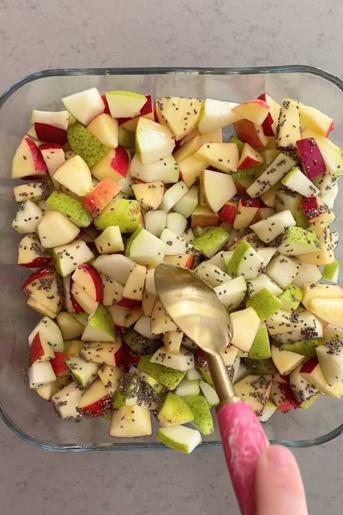 Diced pear and apple tossed with chia seeds in a clear baking dish.