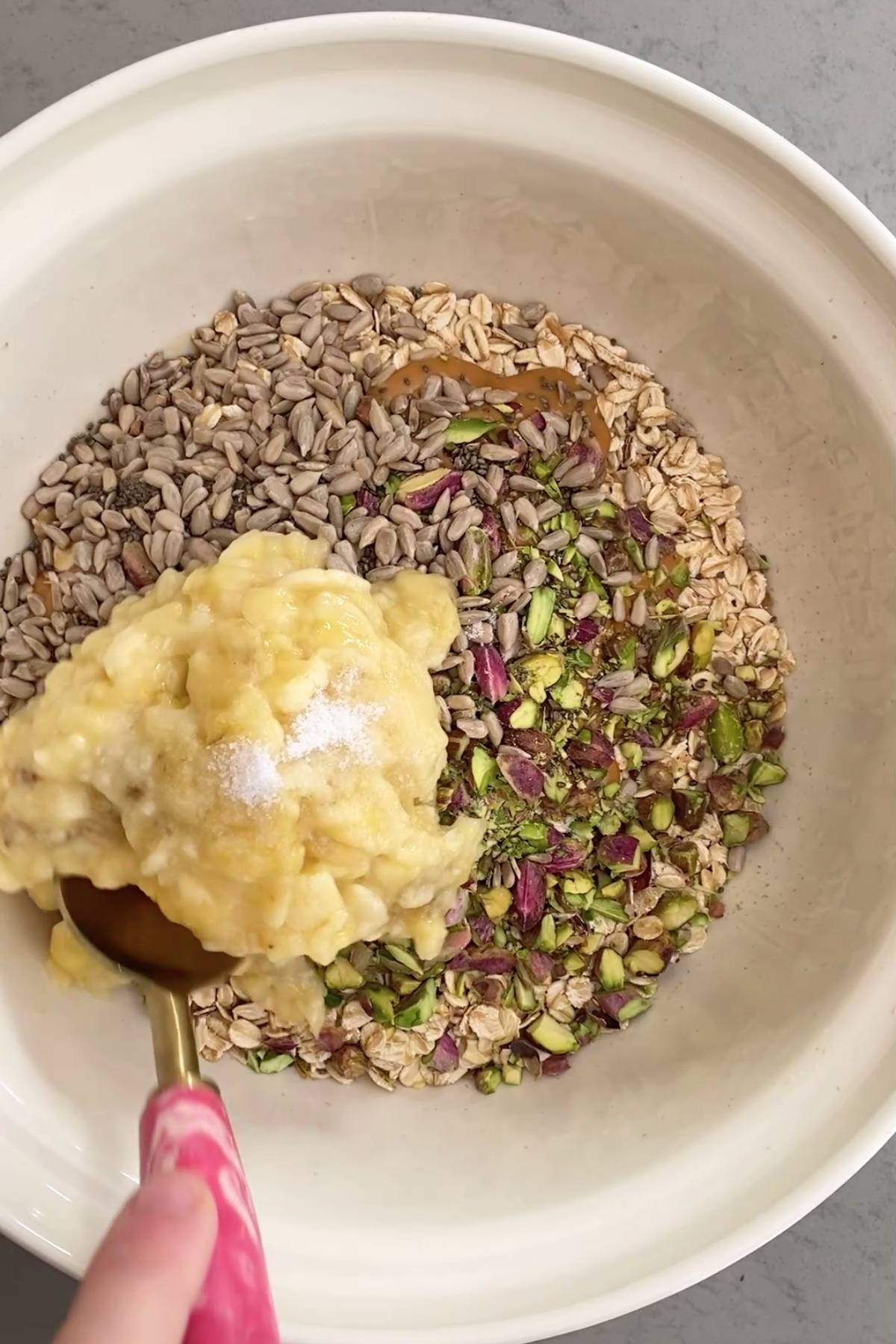 Mixing bowl with oats, sunflower seeds, pistachios, and mashed banana.