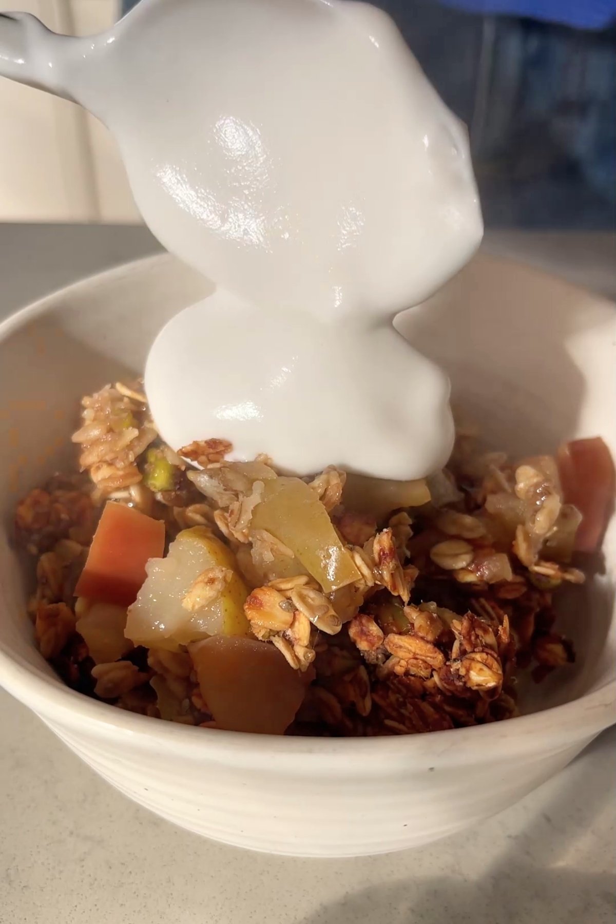 Spoon pouring a dollop of yogurt onto a bowl of fruit crumble.