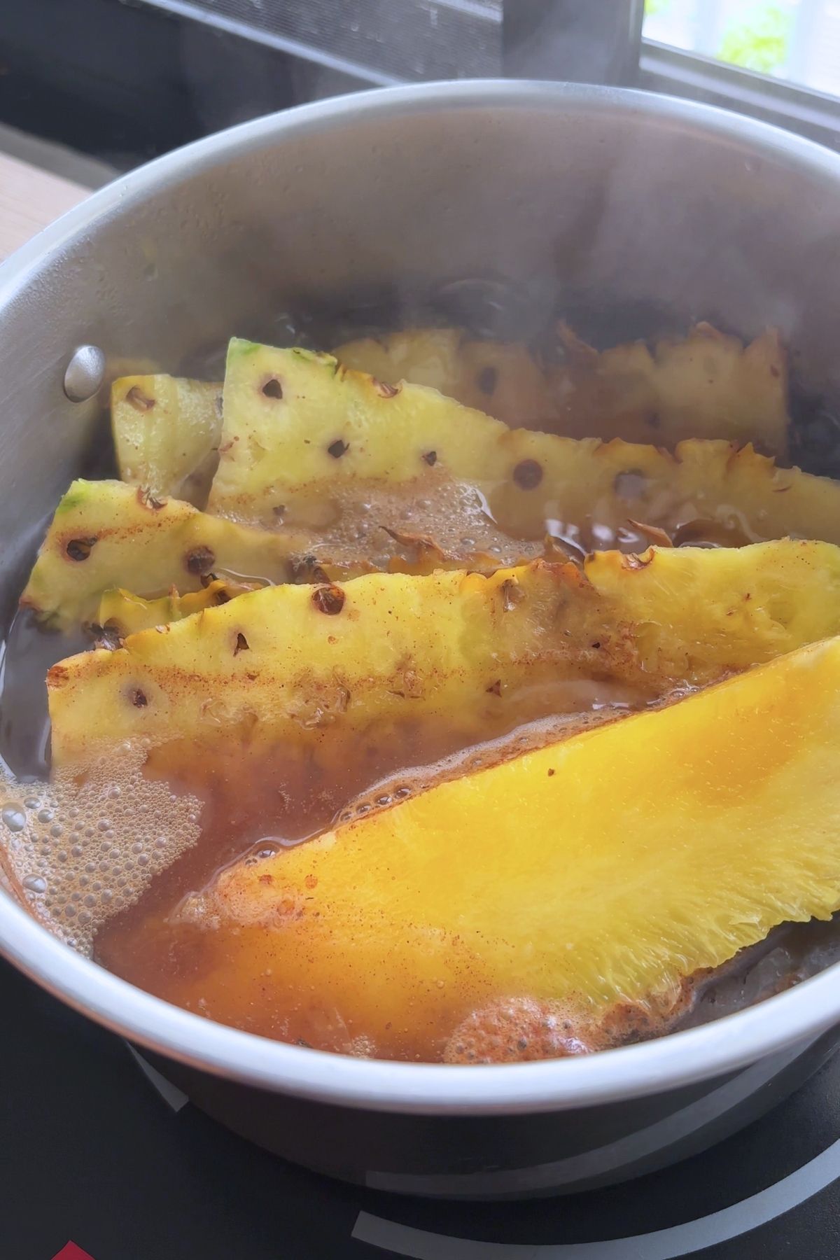 Pineapple peels simmering in spiced tea in a stainless steel pot, steam rising.