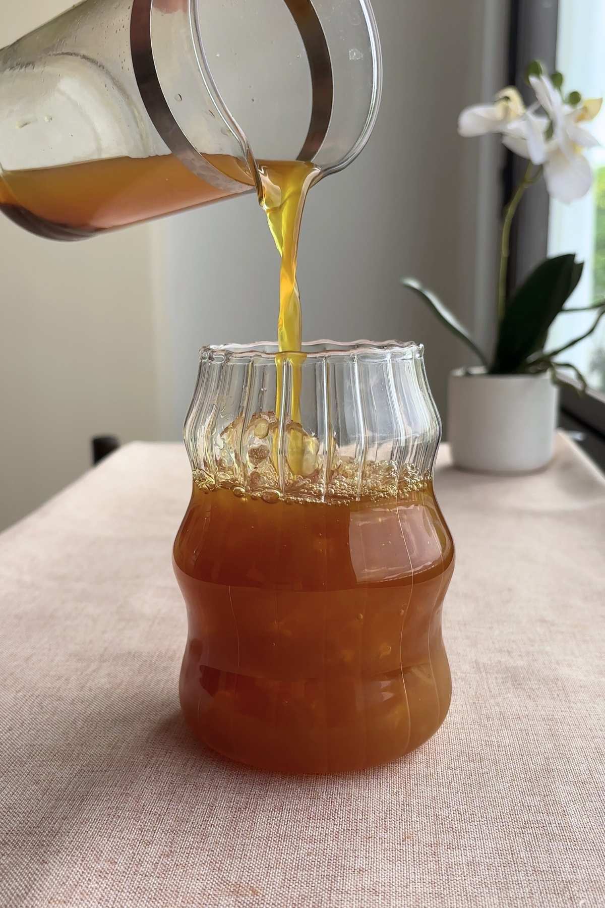 Golden-brown tea pouring into a ridged glass jar.