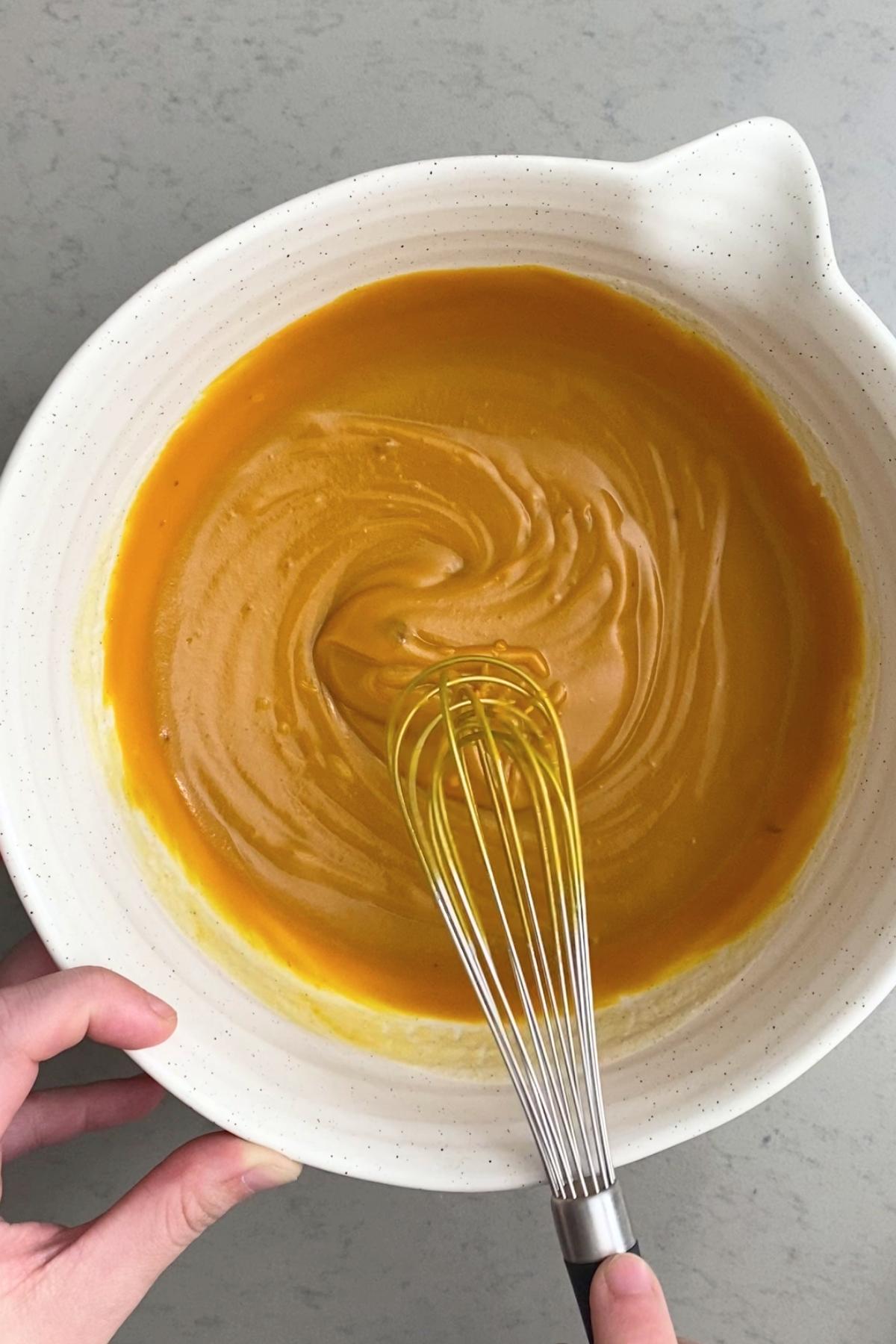 Thick orange pumpkin mixture in a bowl, whipped into a glossy puree around the whisk.