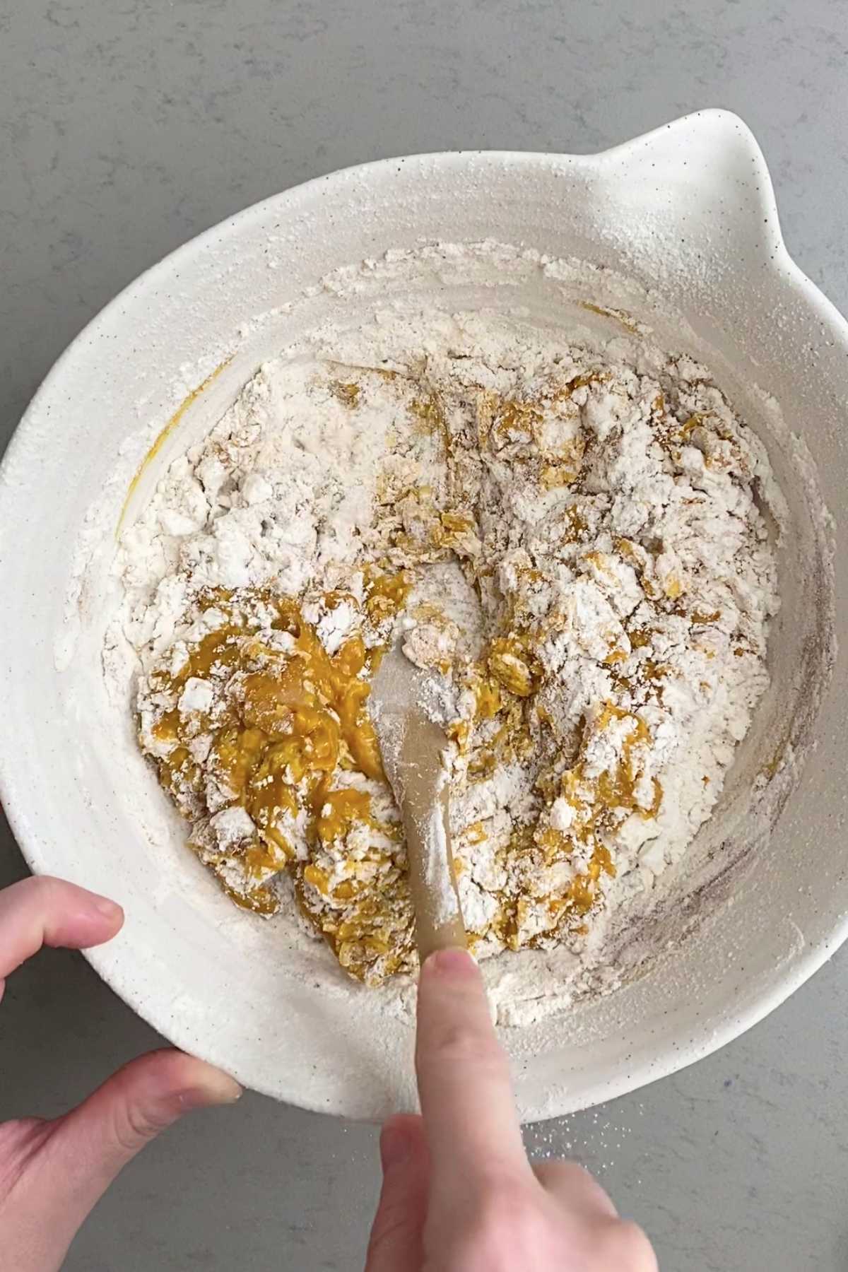 Partially mixed flour and pumpkin batter in a bowl, with a spatula folding the dough.