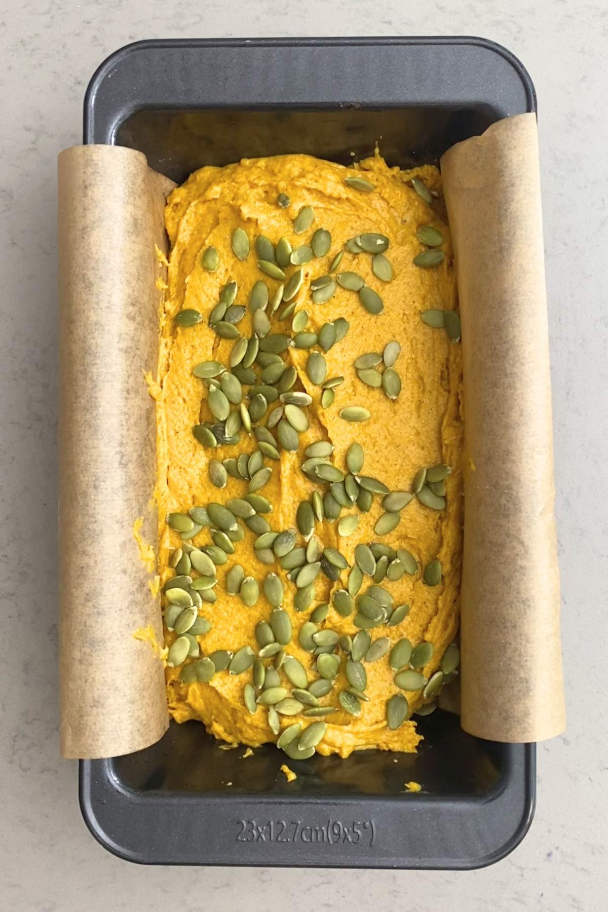 Unbaked pumpkin bread batter smoothed in a parchment-lined loaf pan, topped with pepitas.
