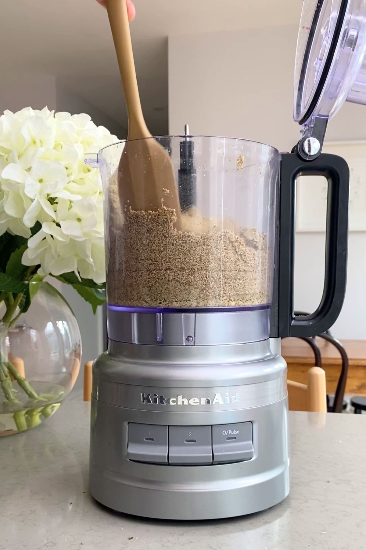 Spatula scraping ground seeds inside a food processor mid-blend.