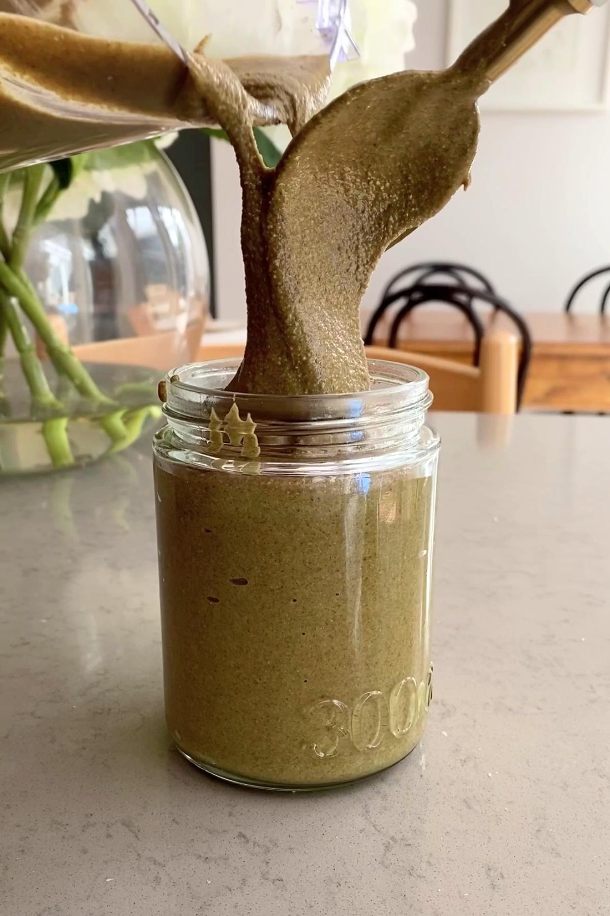 Creamy greenish seed butter pouring from a blender into a jar.