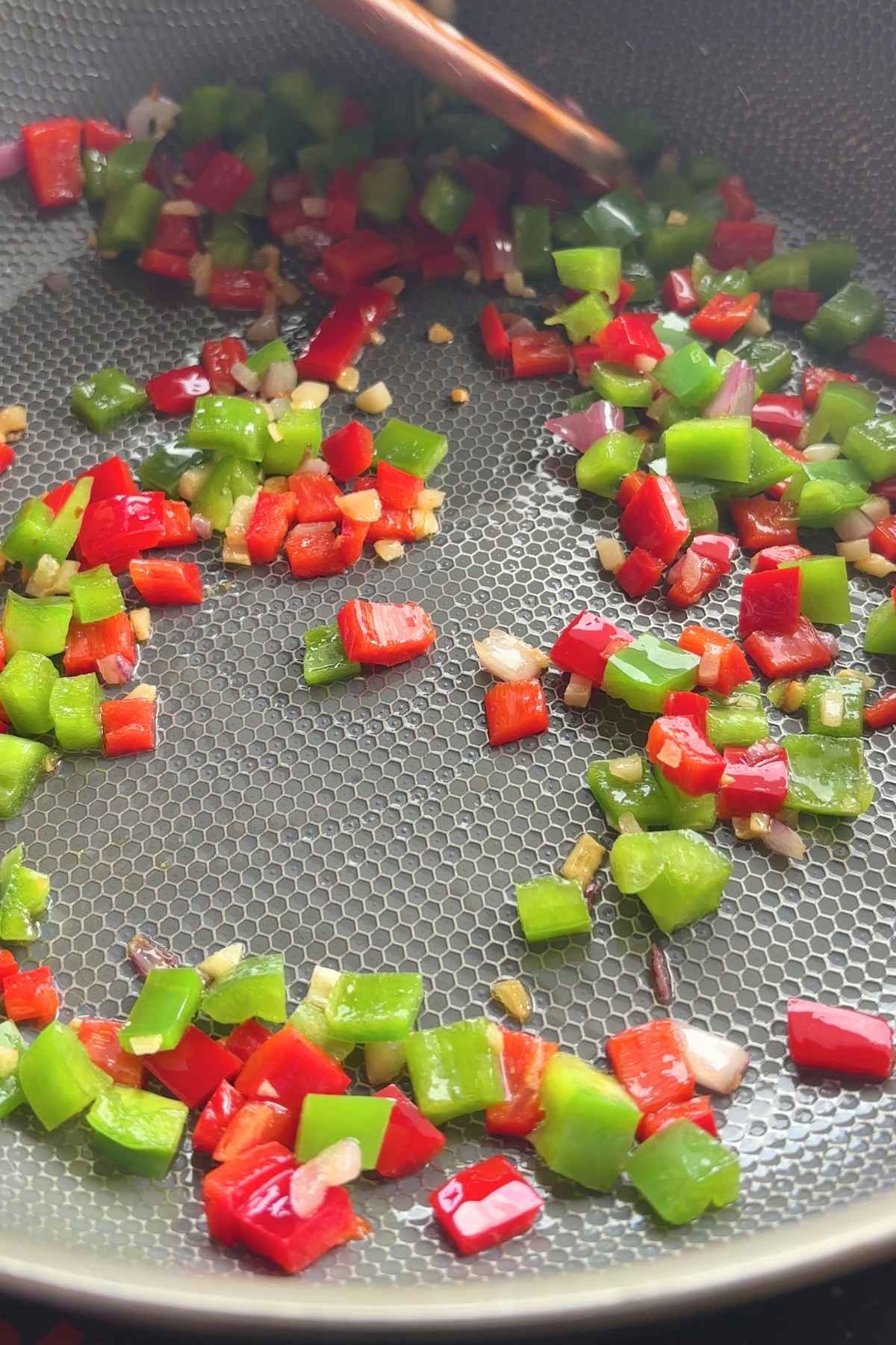 Finely chopped red and green bell peppers with garlic pieces sizzling in a pan.