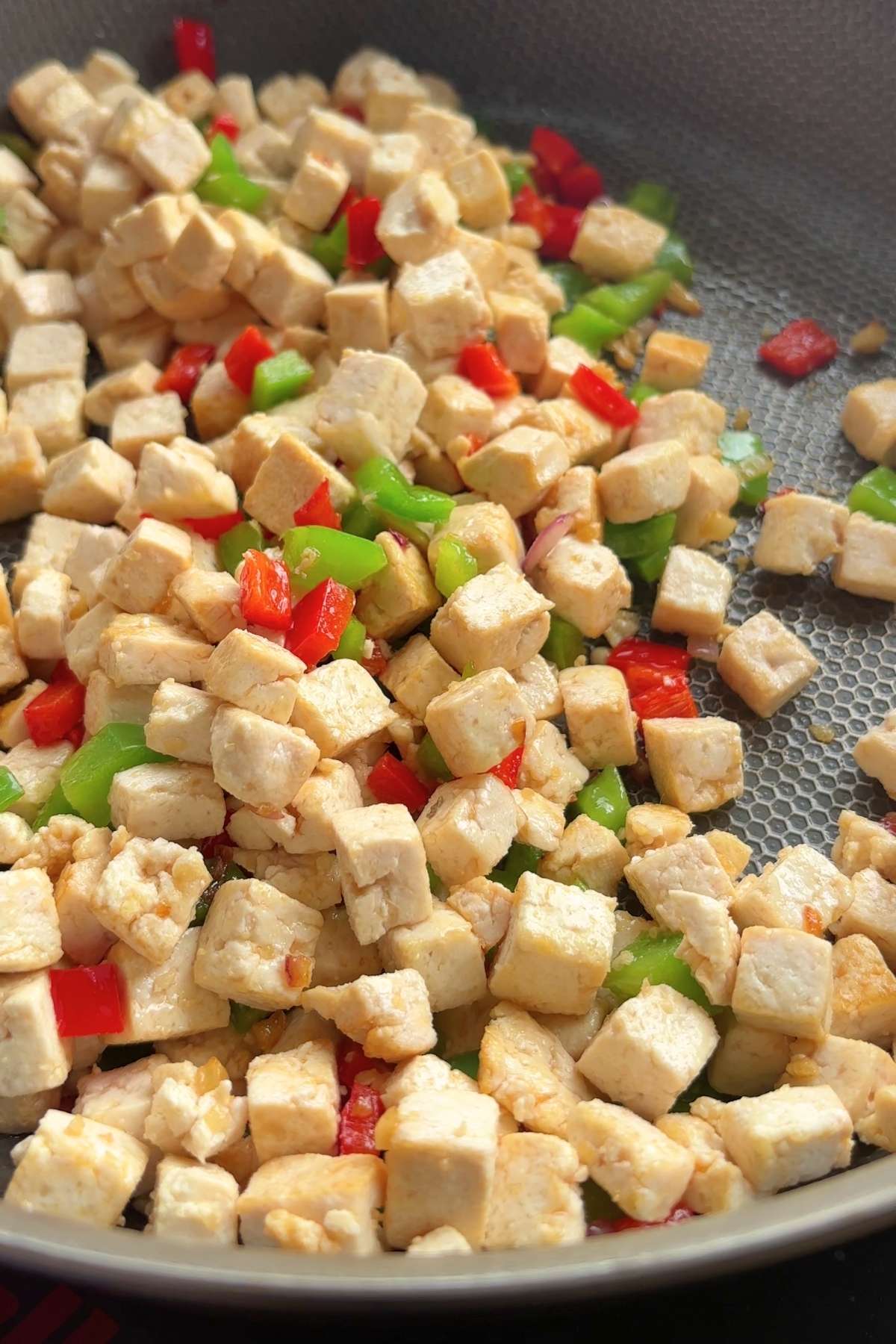 Crispy tofu cubes and diced peppers mixed together in a hot pan.