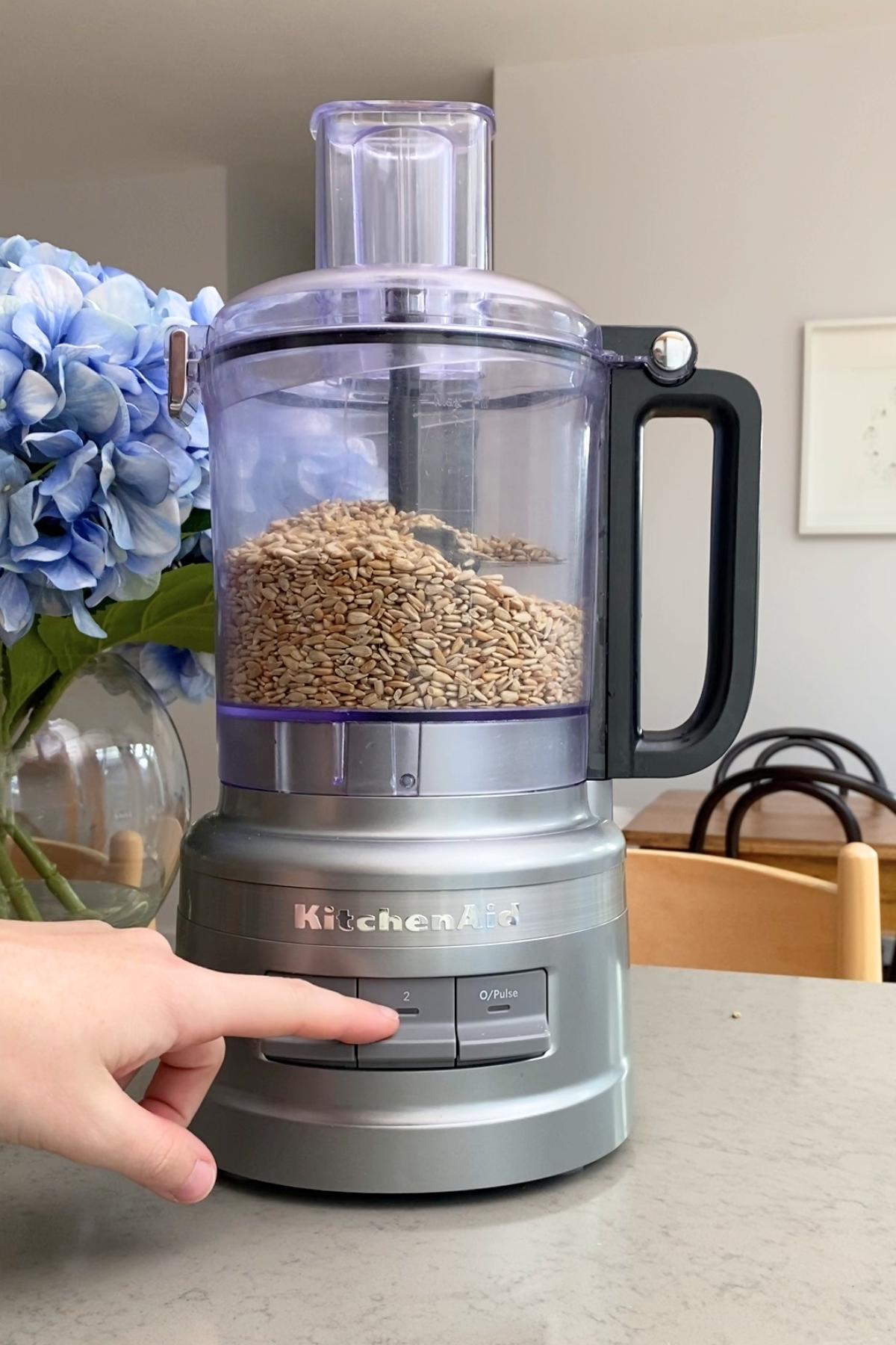 A food processor bowl half-filled with sunflower seeds awaiting blending.