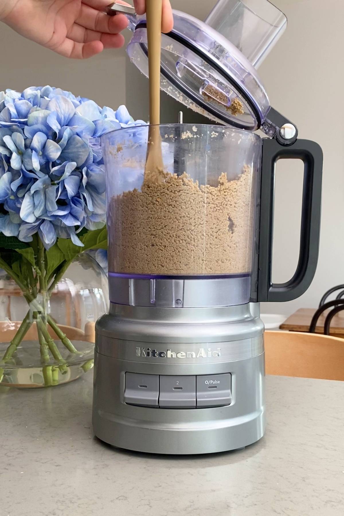 A spatula scraping coarse sunflower seed crumbs from a food processor.