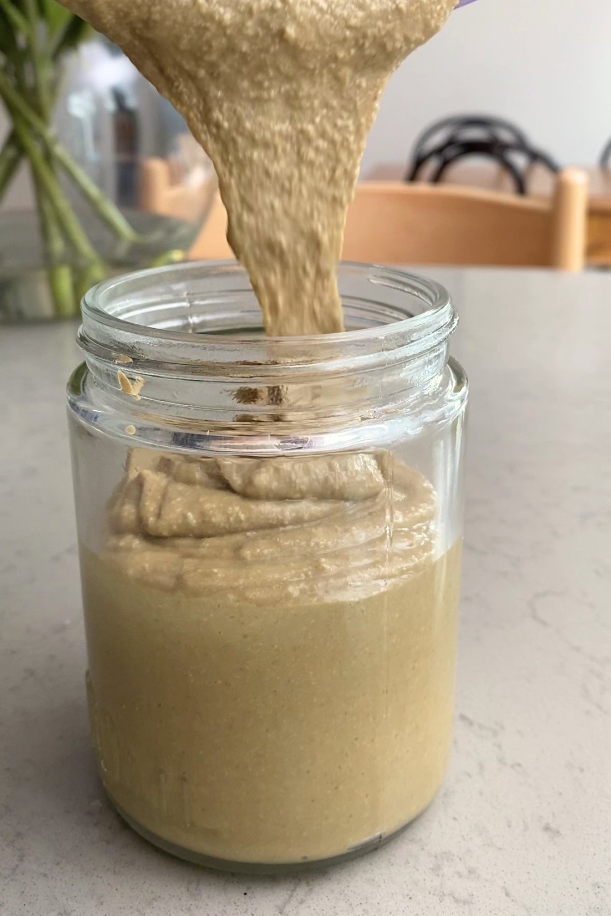 Smooth sunflower seed butter pouring into a glass jar.