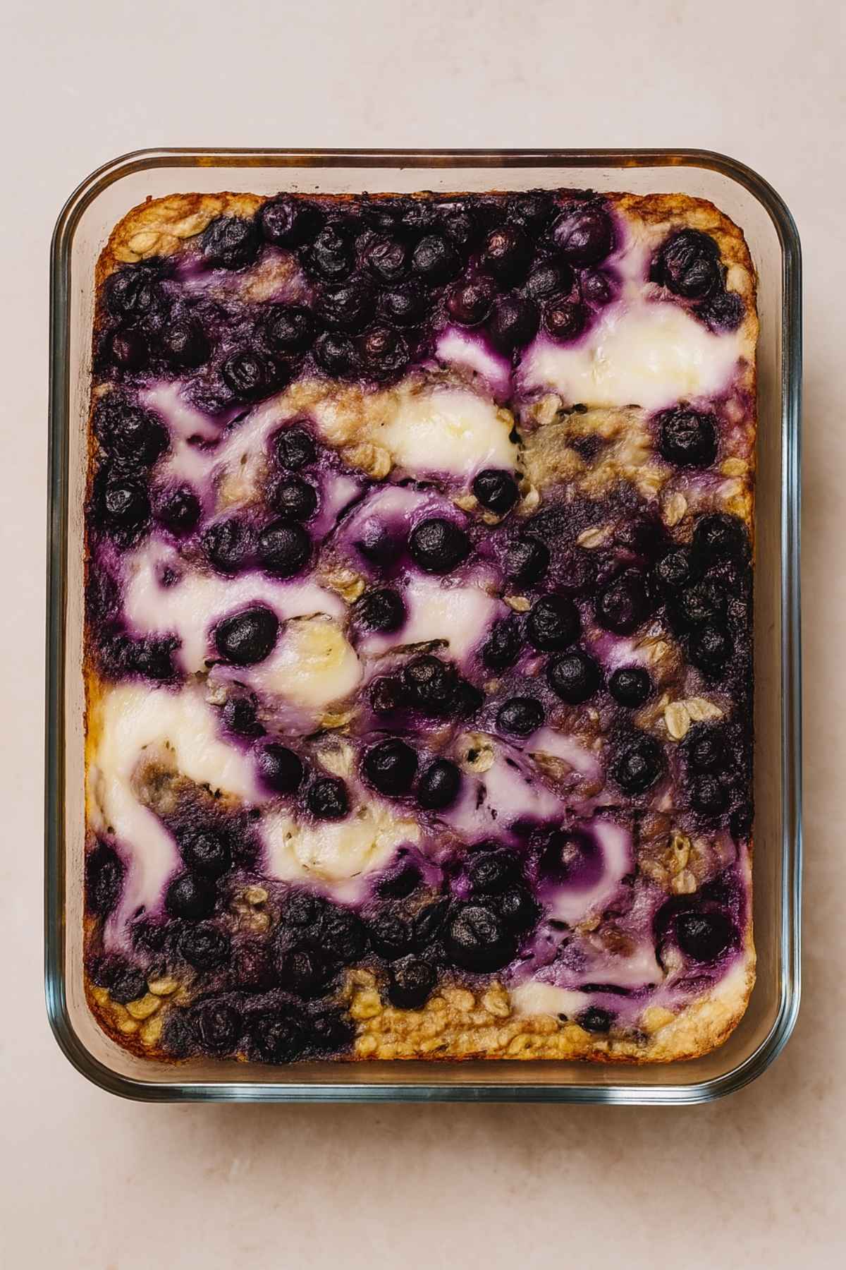 Top-down view of golden baked oats topped with swirled yogurt and baked blueberries in a glass dish.