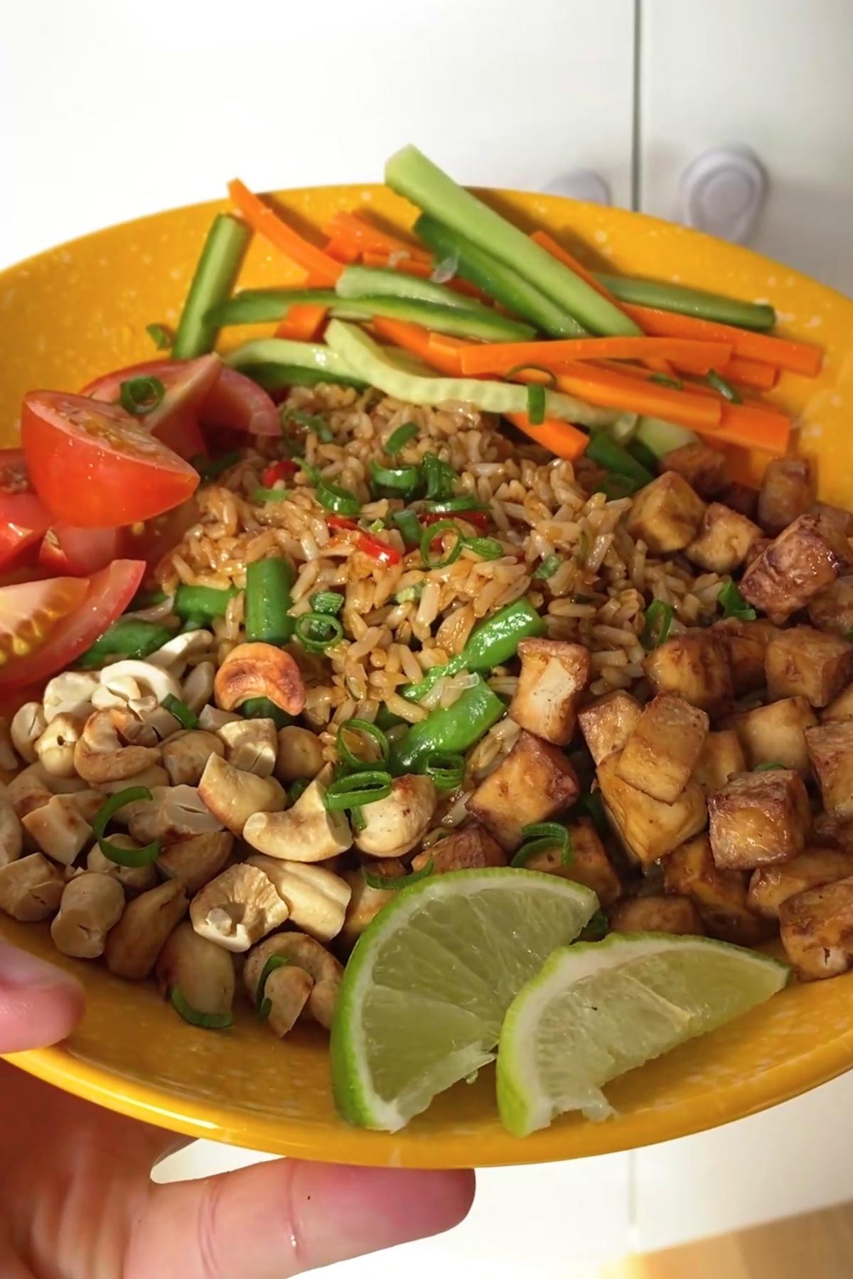Close-up of the finished bowl showing crisp tofu cubes, nuts, and fresh veggies around rice.