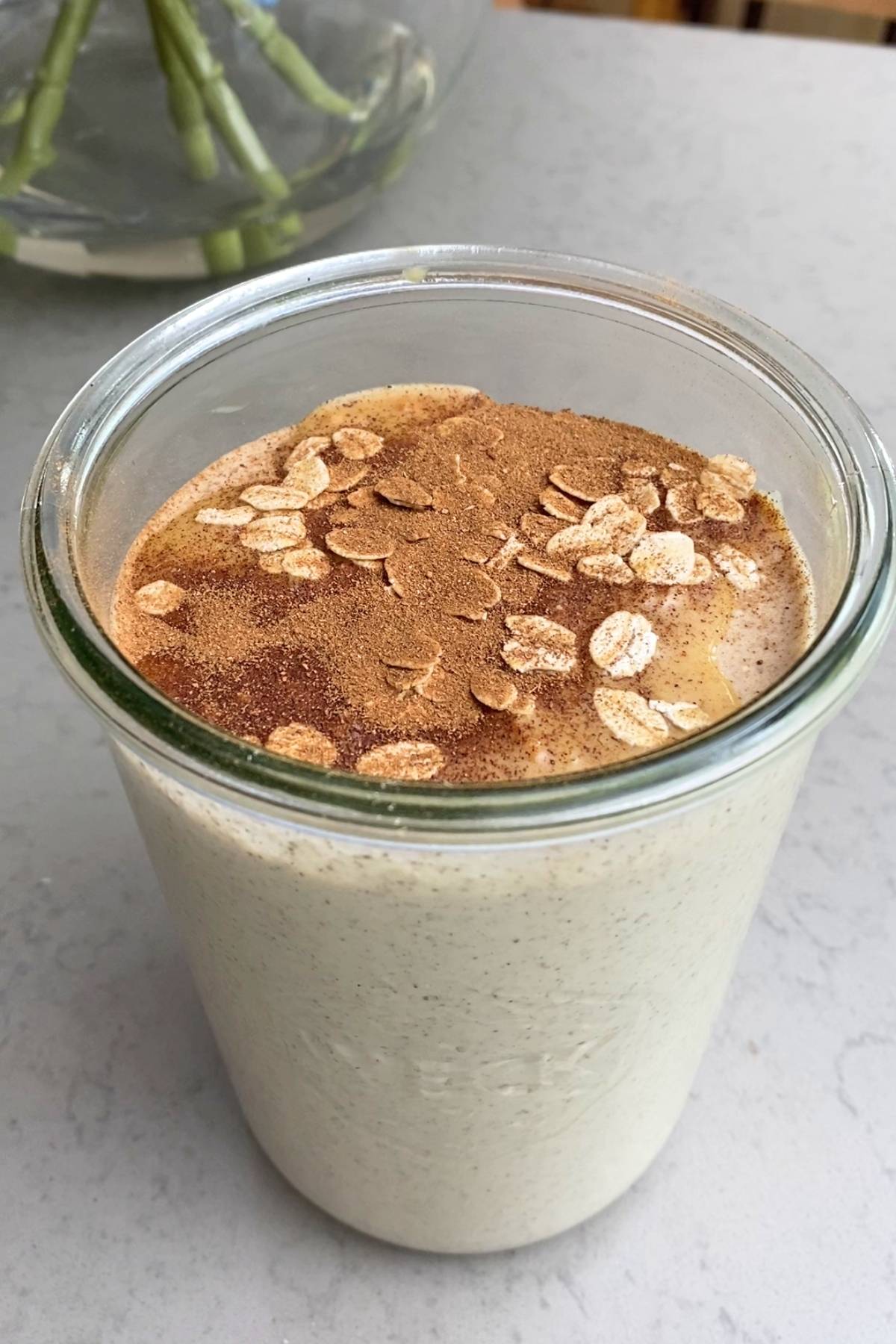 Overhead view of a glass jar with creamy smoothie garnished with oat flakes and cinnamon.