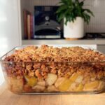 Glass dish filled with golden oat-and-seed topping over bubbling fruit.