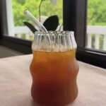 Clear straw angled down into ice-cold pineapple tea in a sculpted glass.